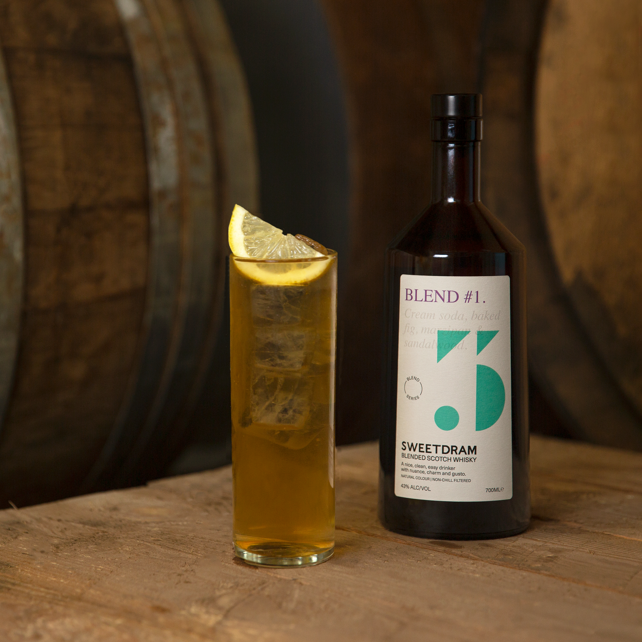 Brown 700ml Blend #1 bottle on pallet next to highball glass of Blended Whisky and Ginger with lemon wedge garnish.