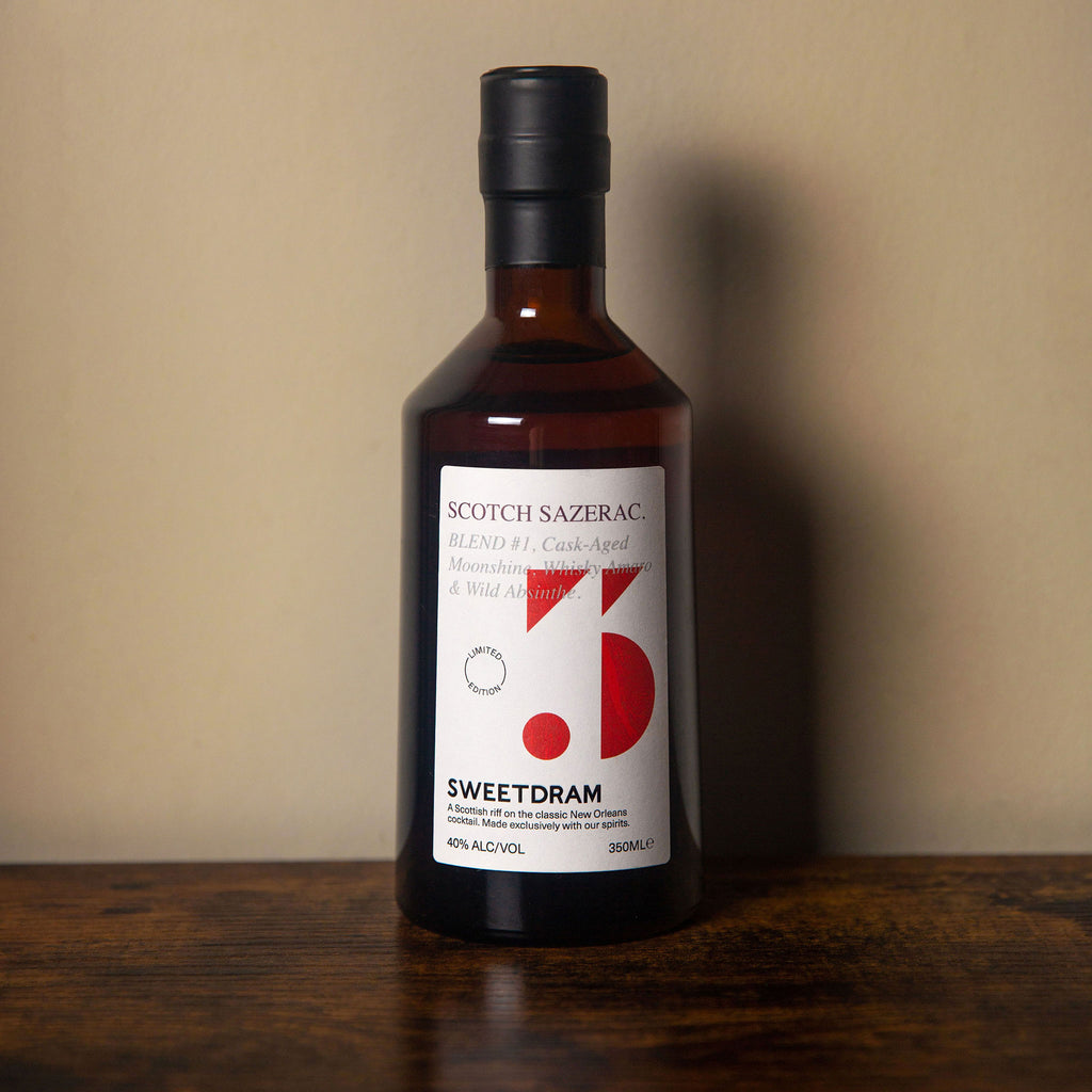 350ml bottle of Scotch Sazerac with red dram logo sitting on a wooden table against a plain beige background.