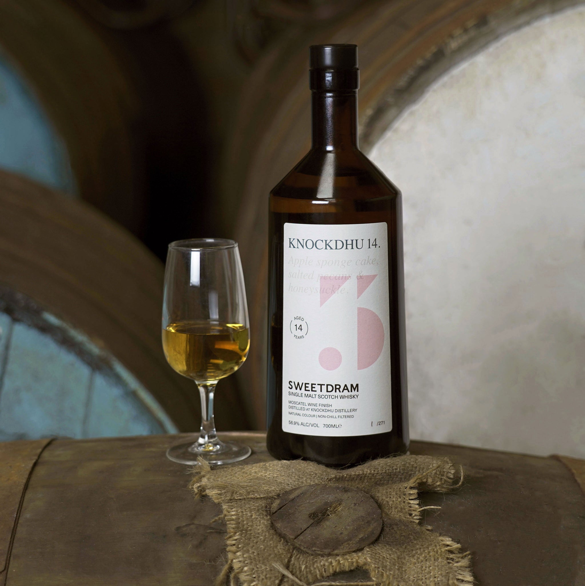 750ml bottle of Knockdhu 14-year-old single-cask Whisky sitting on a cask, with a dram in tasting glass