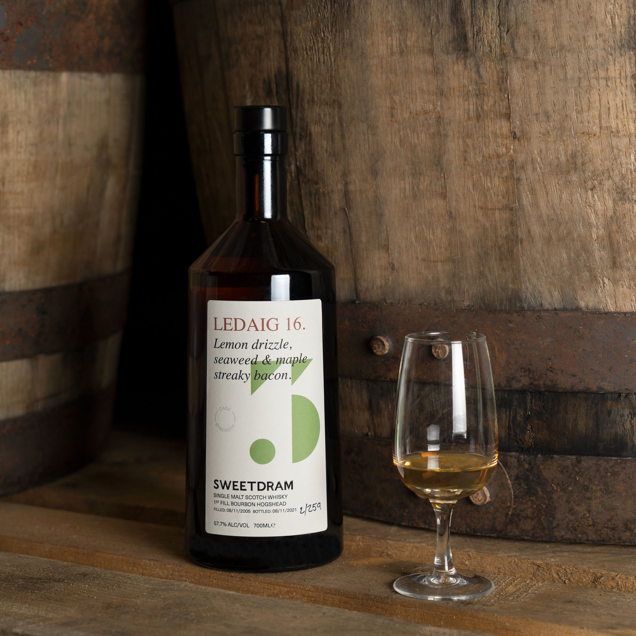 Ledaig 16 bottle with serving glass on top of pallet in front of Sweetdram whisky casks. Brown, natural and warm.